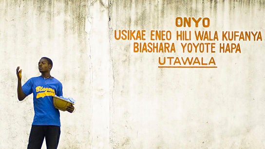 Un vendedor callejero frente a un edificio gubernamental donde se puede leer, en suajili: "Advertencia: no est&aacute; permitido realizar actividades comerciales aqu&iacute;", en Dar es Salaam (Tanzania)