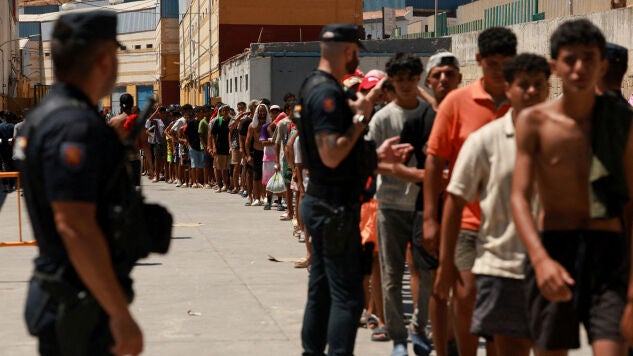 Migrantes hacen cola para recibir alimentos b&aacute;sicos de la ONG local Media Luna Blanca en una zona industrial donde duermen en Ceuta