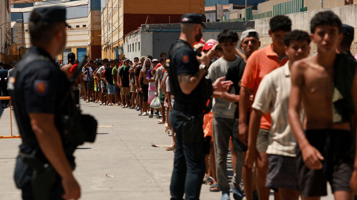 Migrantes hacen cola para recibir alimentos b&aacute;sicos de la ONG local Media Luna Blanca en una zona industrial donde duermen en Ceuta