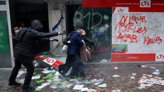 Varias personas salen por el escaparate roto de una tienda para evacuar el edificio, durante los enfrentamientos posteriores a una manifestaci&oacute;n en Par&iacute;s
