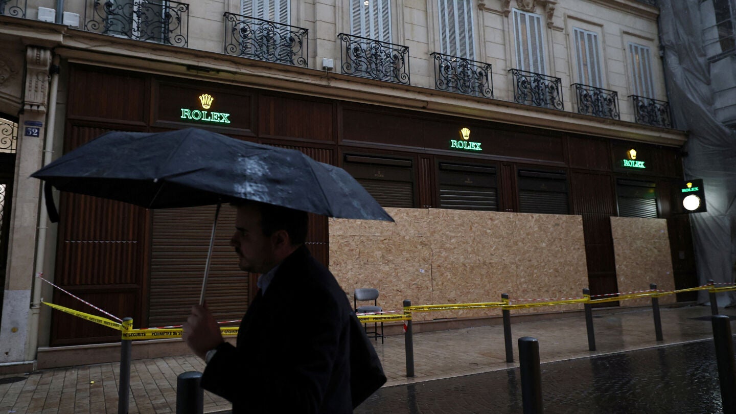Un hombre se protege de la lluvia bajo un paraguas mientras pasa frente a una tienda vandalizada, en Francia, el 19 de octubre de 2026.