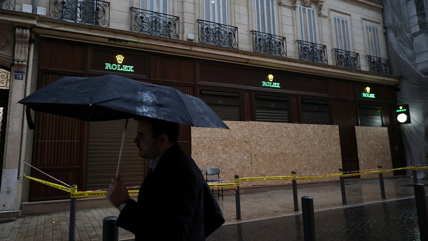 Un hombre se protege de la lluvia bajo un paraguas mientras pasa frente a una tienda vandalizada, en Francia, el 19 de octubre de 2026. Un hombre se protege de la lluvia bajo un paraguas mientras pasa frente a una tienda vandalizada, en Francia, el 19 de octubre de 2026.