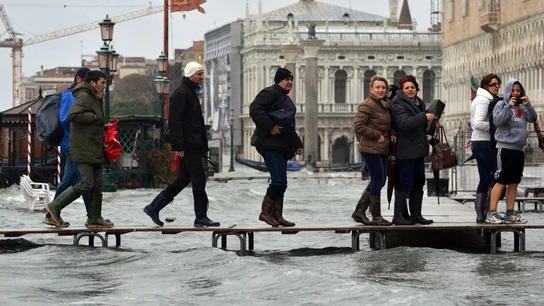 Varias personas caminan por un puente improvisado en Venecia, Italia, inundada por la marea alta. Varias personas caminan por un puente improvisado en Venecia, Italia, inundada por la marea alta.