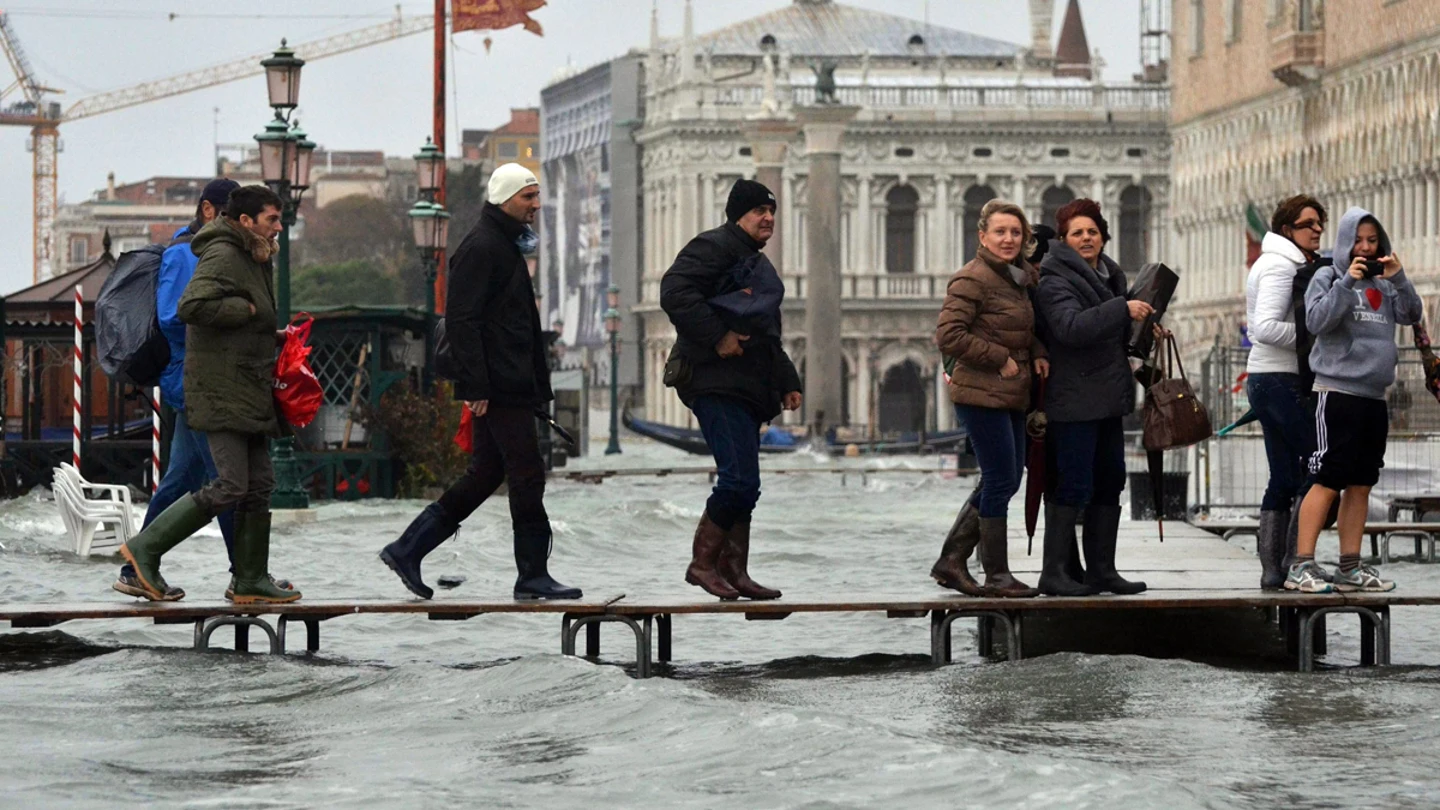 Varias personas caminan por un puente improvisado en Venecia, Italia, inundada por la marea alta. Varias personas caminan por un puente improvisado en Venecia, Italia, inundada por la marea alta.