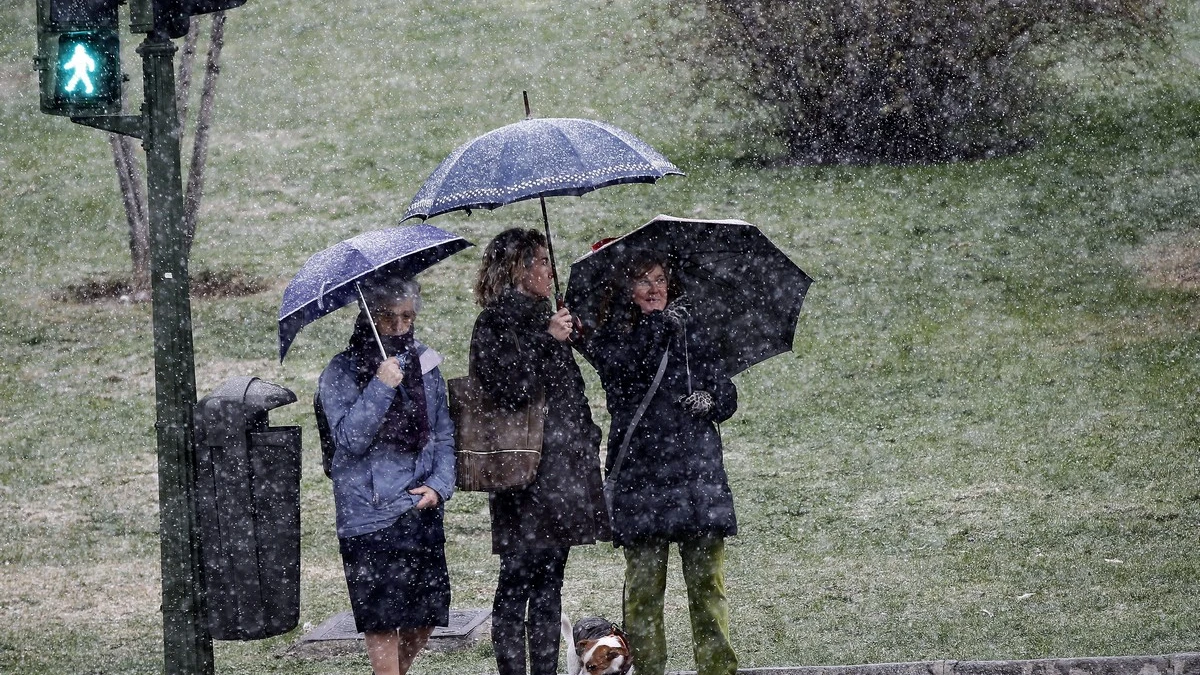 Tres viandantes se protegen con paraguas de la nieve que ha comenzado a caer en la capital.