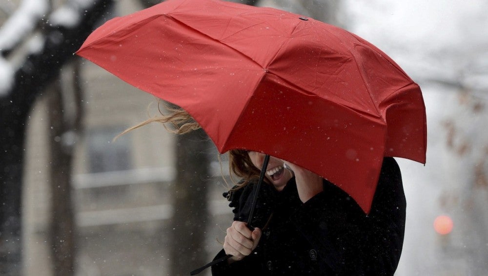 Una mujer habla por su teléfono móvil tratando de protegerse del viento