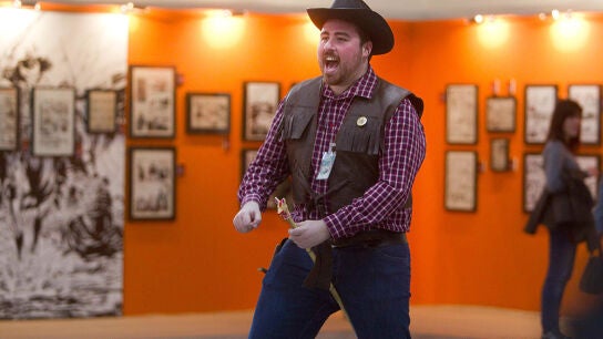 Un hombre disfrazado de cowboy pasea con su particular caballo de madera