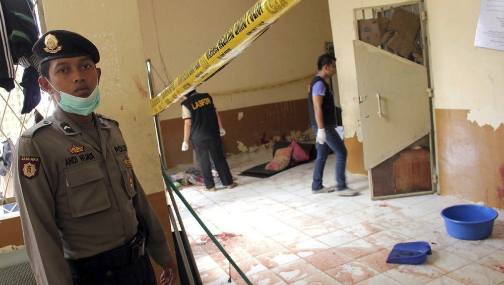 Un policía indonesio vigila mientras varios policías forenses revisan el lugar de un suceso.