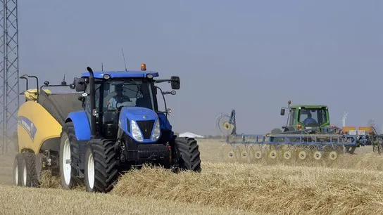 Una empacadora junto a una hileradora trabajan en un campo de cereal Una empacadora junto a una hileradora trabajan en un campo de cereal