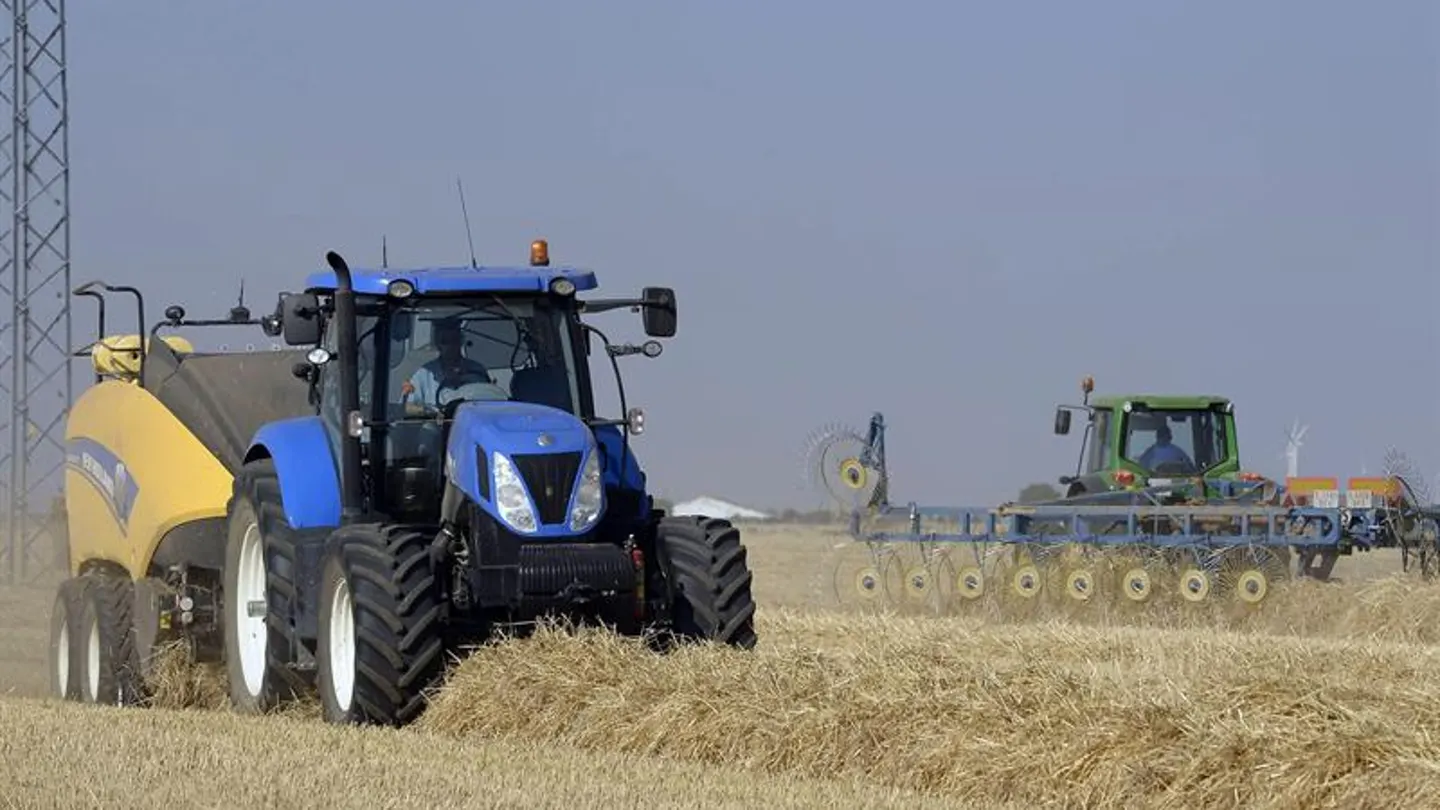 Una empacadora junto a una hileradora trabajan en un campo de cereal Una empacadora junto a una hileradora trabajan en un campo de cereal