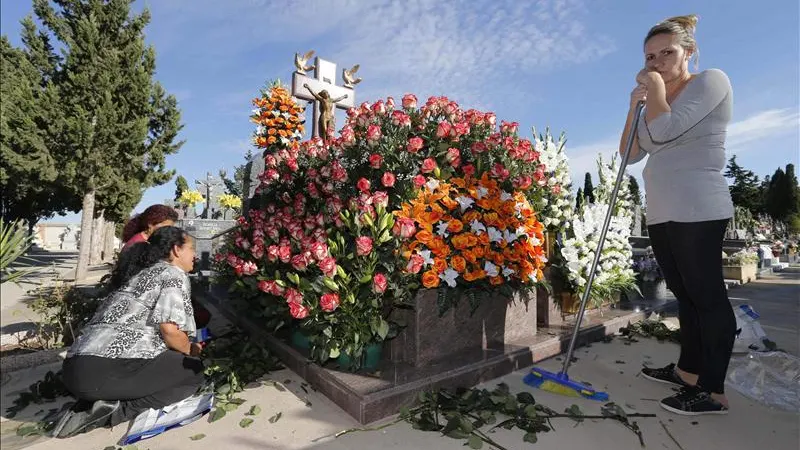 Varias mujeres colocan flores en la tumba de un familiar en el cementerio