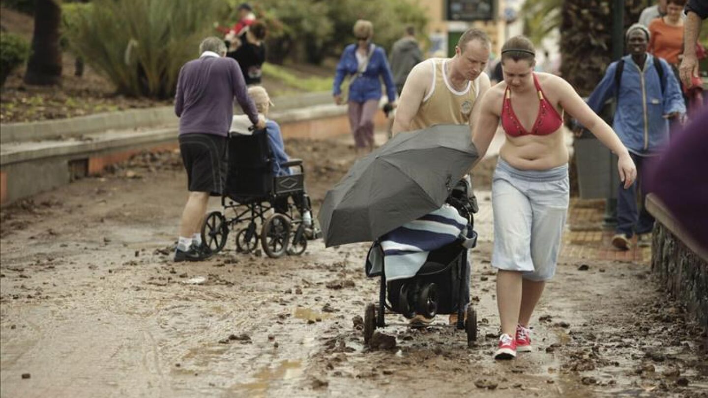 Unos turistas tratan de sortear el barro acumulado en un paseo de la ciudad de Los Cristianos