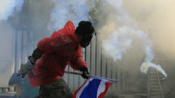 Un manifestante lanza gas lacrimógeno contra una barricada de la policía