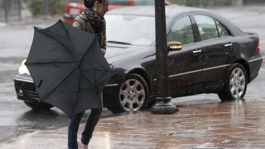 Una mujer tiene dificultades con su paraguas en una jornada de lluvia y viento Una mujer tiene dificultades con su paraguas en una jornada de lluvia y viento