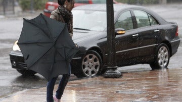 Una mujer tiene dificultades con su paraguas en una jornada de lluvia y viento