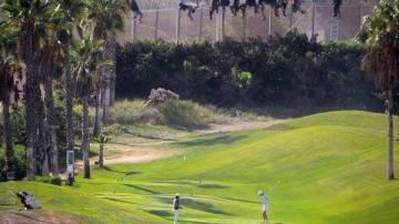 Inmigrantes en la valla de Melilla mientras varias personas juegan al golf