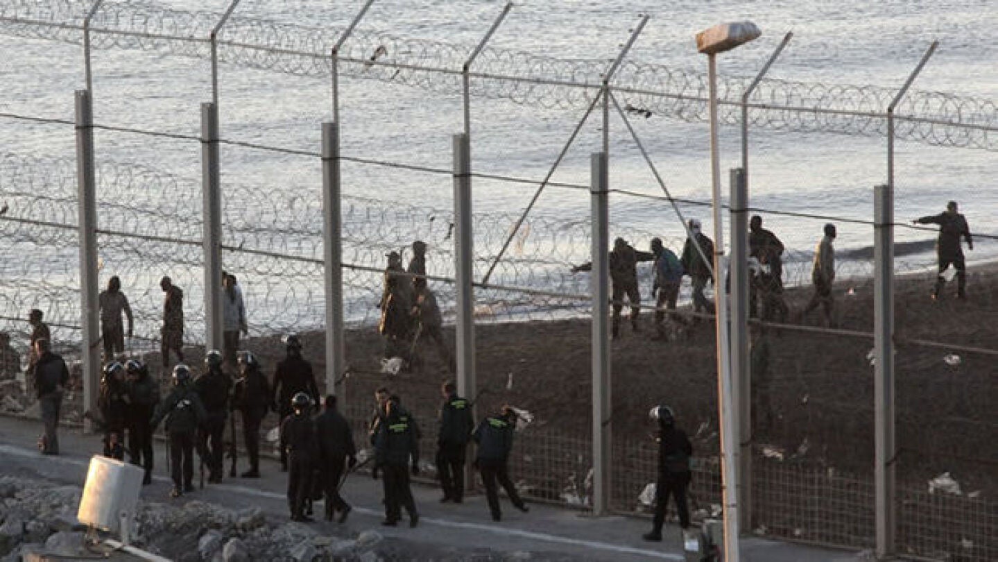 Las fuerzas espa&ntilde;olas de seguridad e inmigrantes a ambos lado de la valla de Ceuta