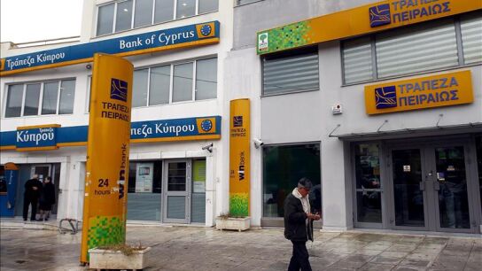 Un hombre pasa junto a una sucursal del Banco de Chipre y del Banco Piraeus, en Atenas