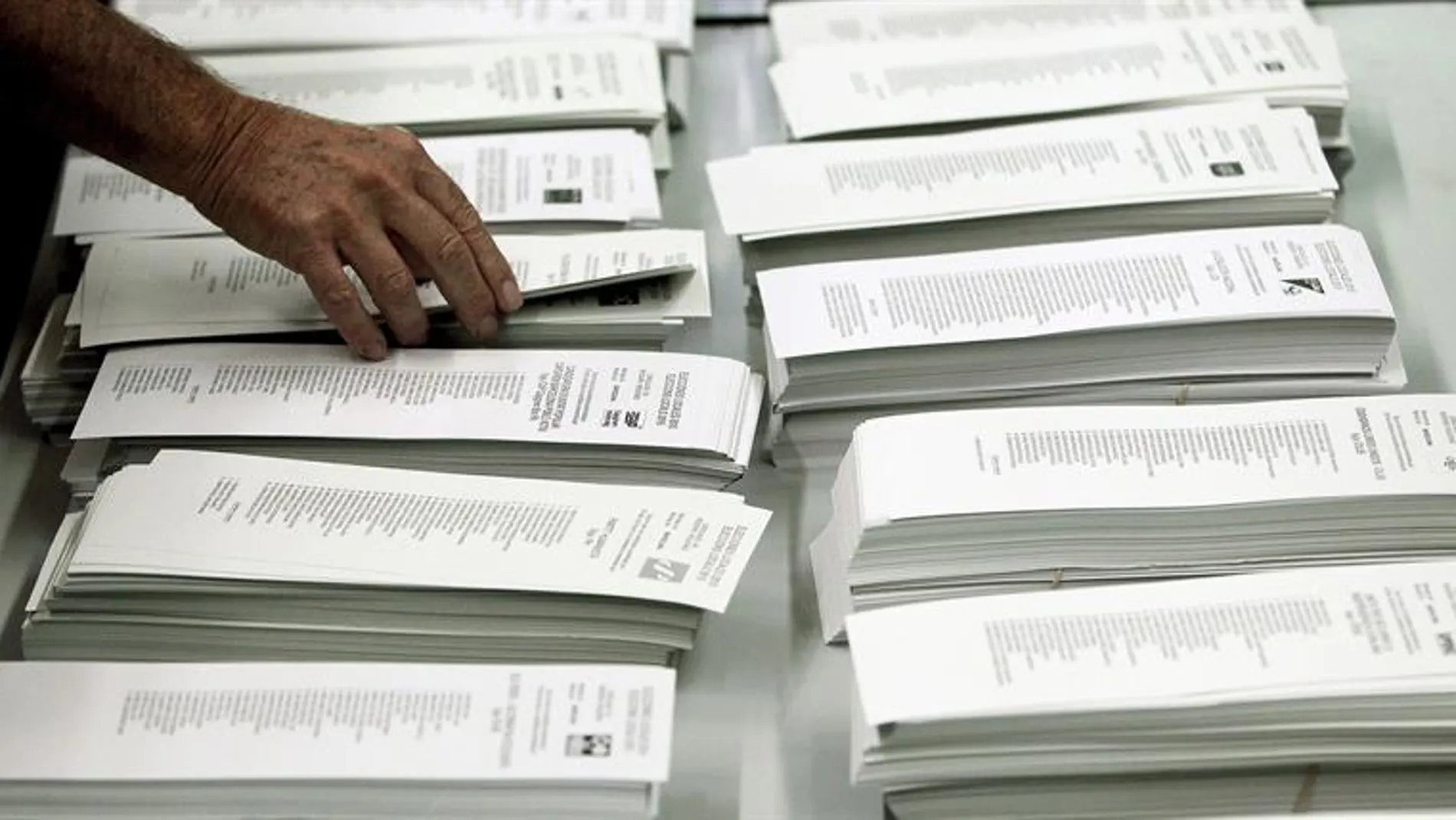 Un ciudadano coge una papeleta de una cabina en un colegio electoral 