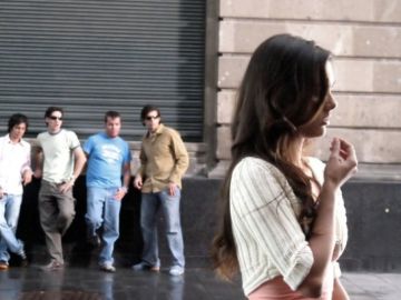 Un grupo de hombres observa a una mujer en la vía pública. Un grupo de hombres observa a una mujer en la vía pública.