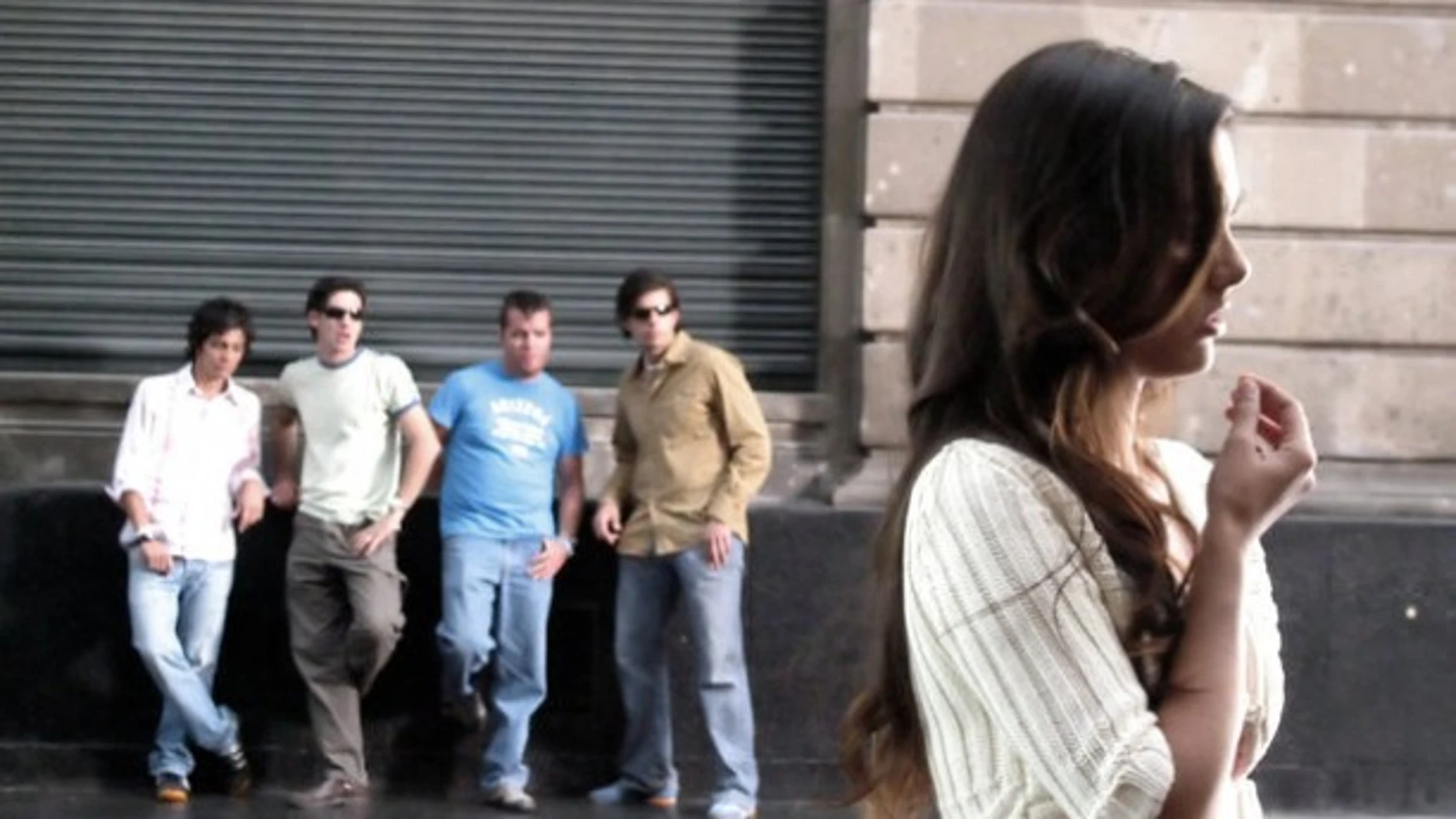 Un grupo de hombres observa a una mujer en la vía pública.