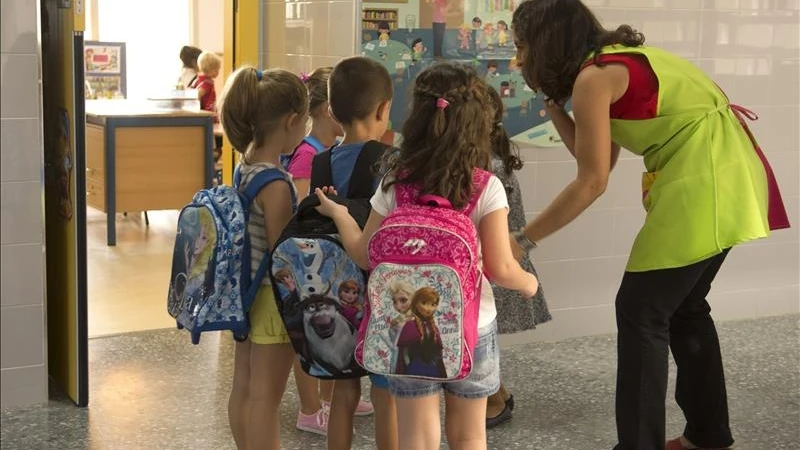 Varios niños entran al colegio con su profesora Varios niños entran al colegio