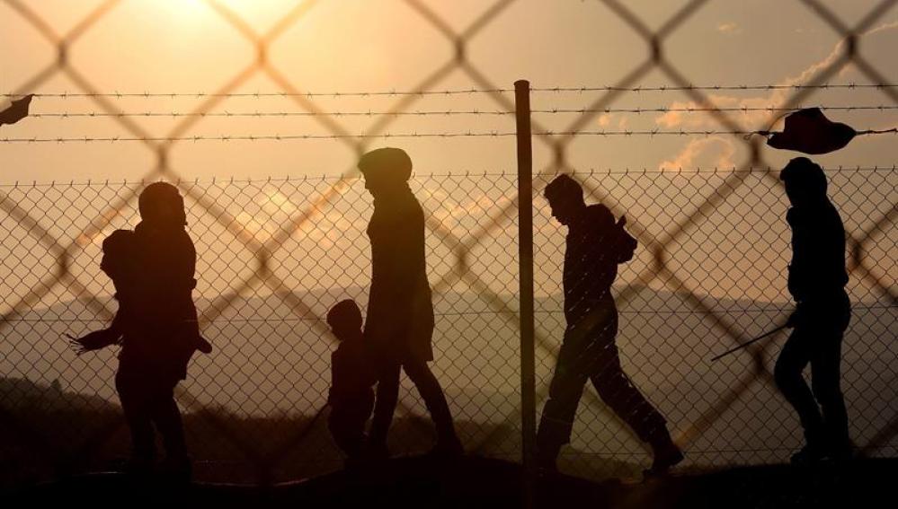Varios inmigrantes caminan alrededor de una valla