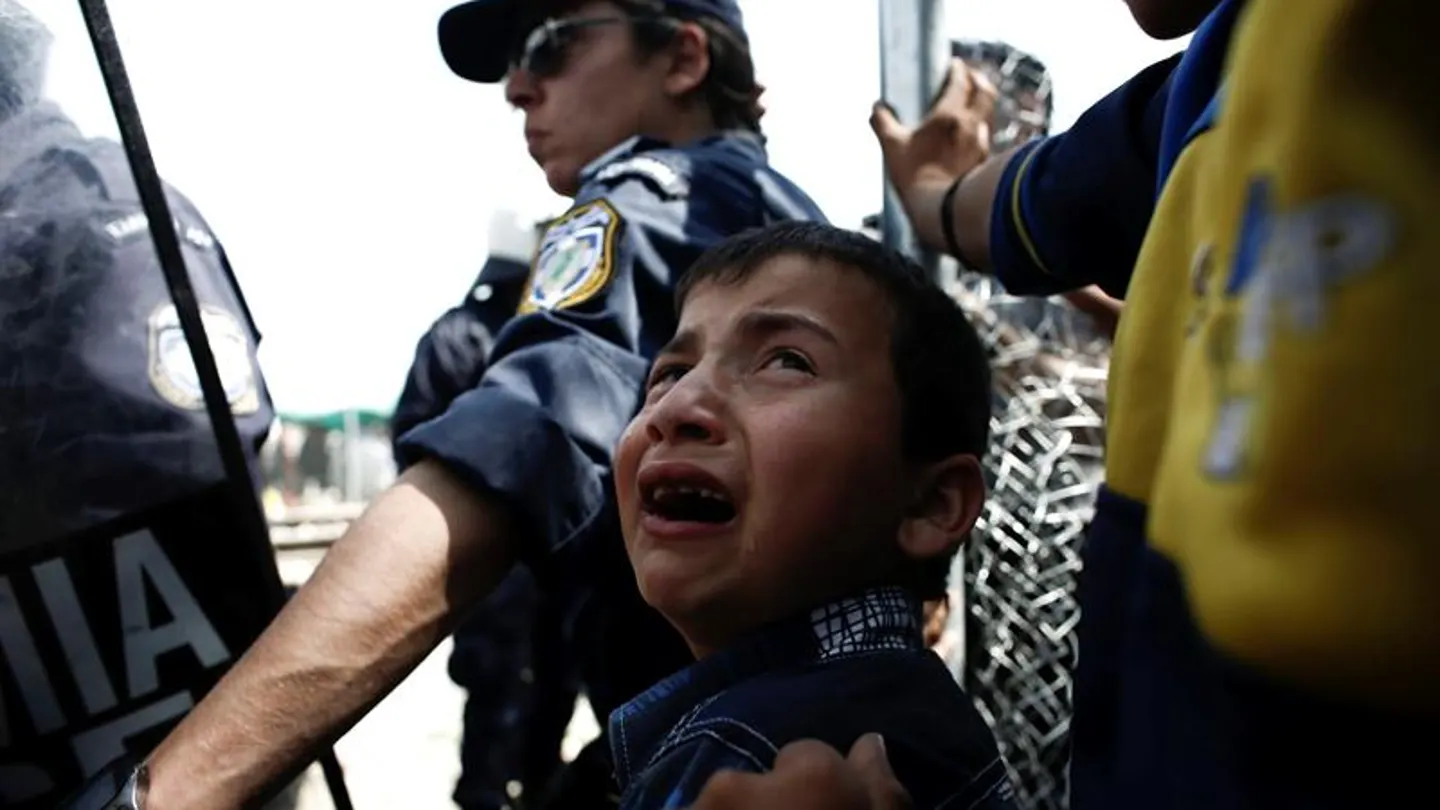 Un niño refugiado llora junto a un Policía Un niño refugiado llora junto a un Policía