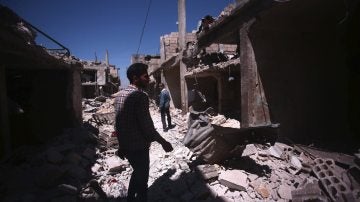 Varias personas caminan sobre los escombros de los edificios destruidos durante unos bombardeos