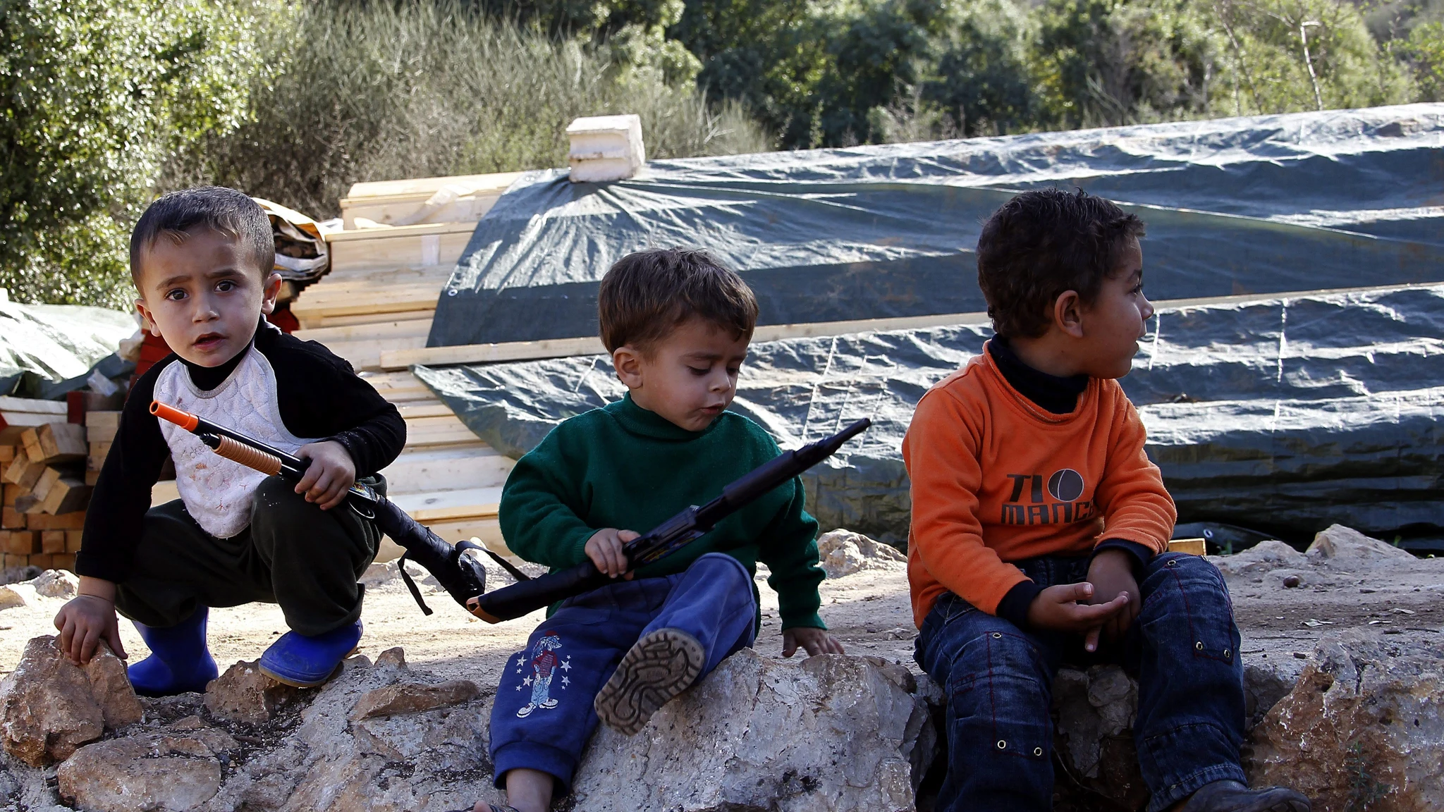 Niños sirios sostienen armas de juguete en un campo de refugiados