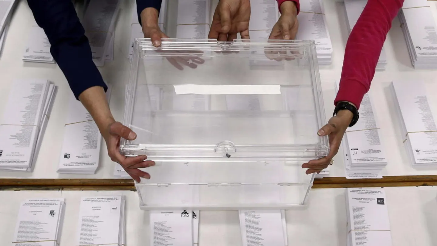 Varias manos sujetando una urna sobre las papeletas de unas elecciones Urnas electorales