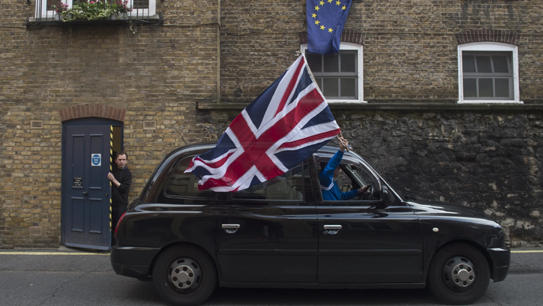 Un taxista ondea una bandera británica en una calle con una bandera europea