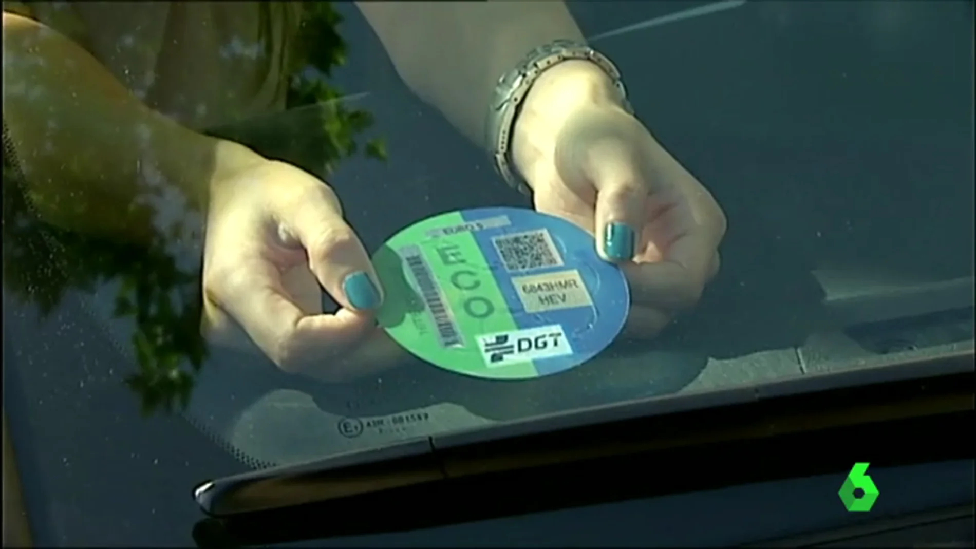 Una conductora coloca el sello 'eco' en la luna de su vehículo ecológico