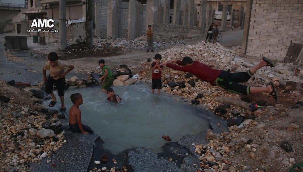 Un grupo de niños sirios juega en torno al cráter de una bomba convertido en piscina en Alepo