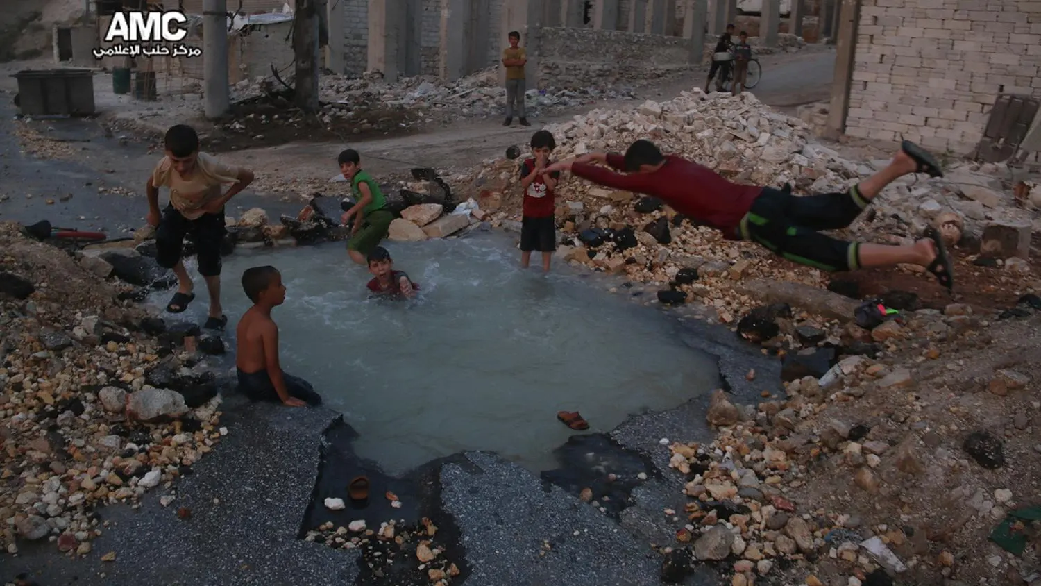 Un grupo de niños sirios juega en torno al cráter de una bomba convertido en piscina en Alepo