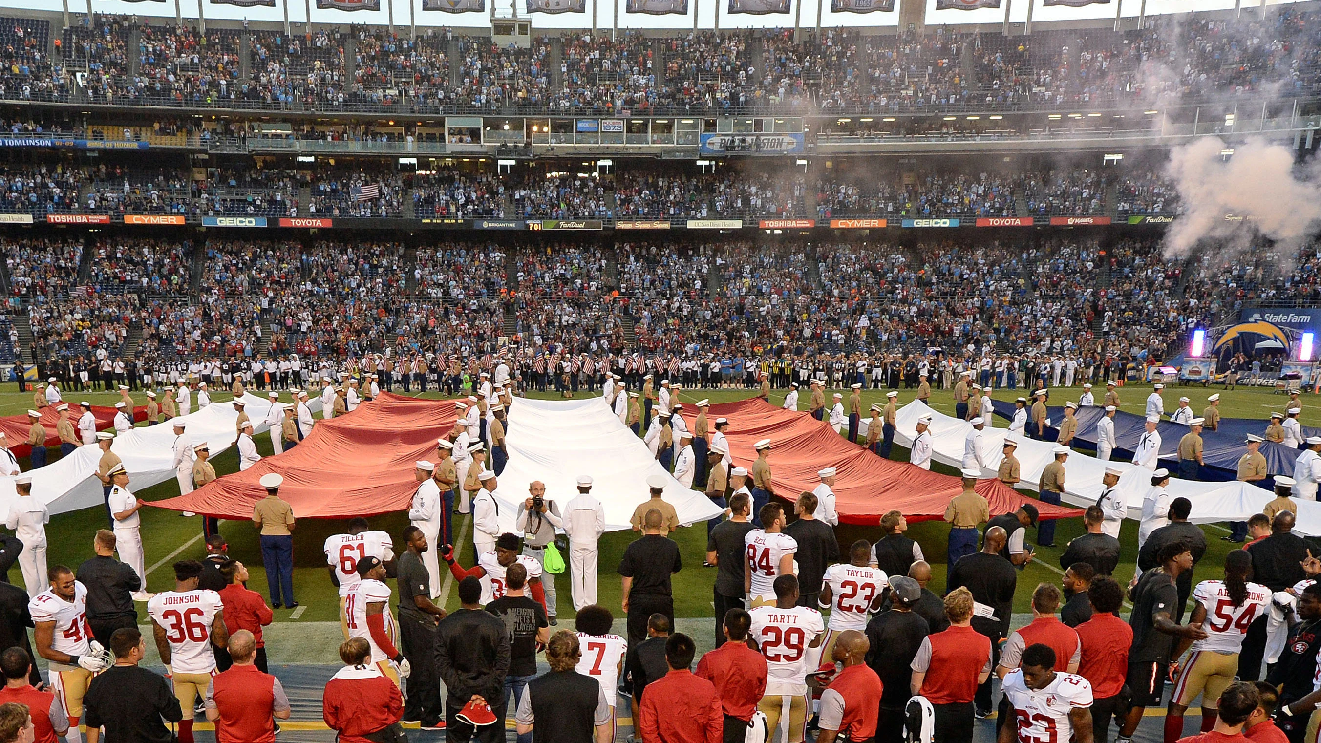 Colin Kaepernick, en la parte inferior de la fotografía (lleva el dorsal 7), de rodillas mientras suena el himno de Estados Unidos