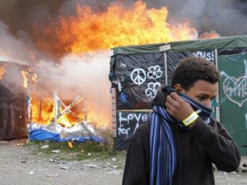 Un migrante se protege el rostro al pasar junto a chabolas en llamas durante el desmantelamiento del campamento conocido como la 'Jungla' de Calais Un migrante se protege el rostro al pasar junto a chabolas en llamas durante el desmantelamiento del campamento conocido como la 'Jungla' de Calais