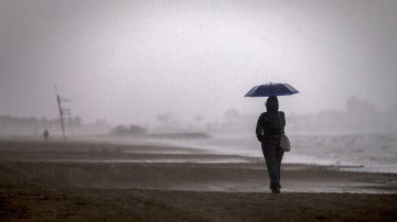 Una persona pasea por la playa de la Malvarrosa bajo la lluvia