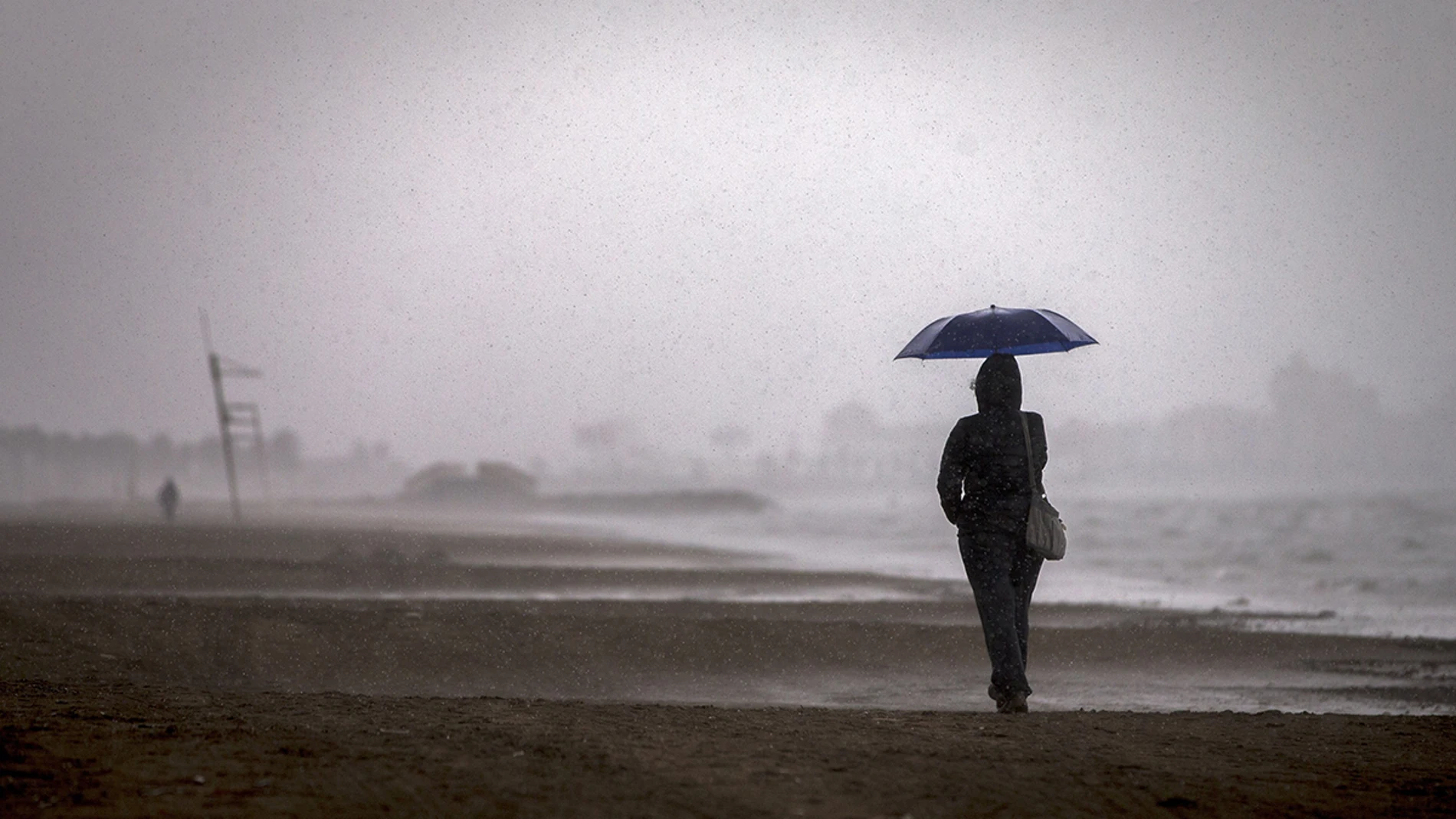 Una persona pasea por la playa de la Malvarrosa bajo la lluvia