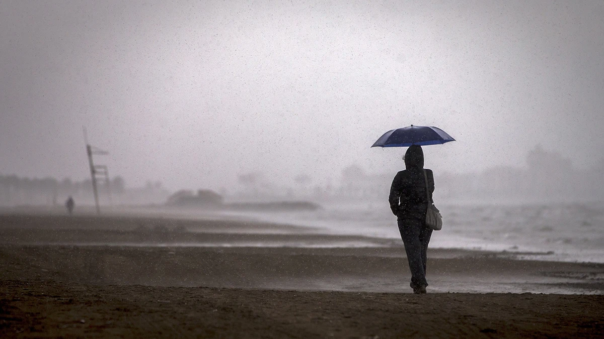 Una persona pasea por la playa de la Malvarrosa bajo la lluvia