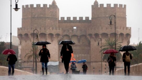 Varias personas cruzan el puente de Serranos, Valencia, bajo la lluvia