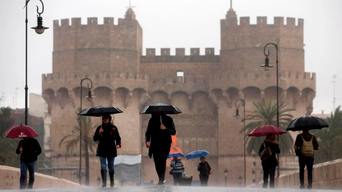 Varias personas cruzan el puente de Serranos, Valencia, bajo la lluvia