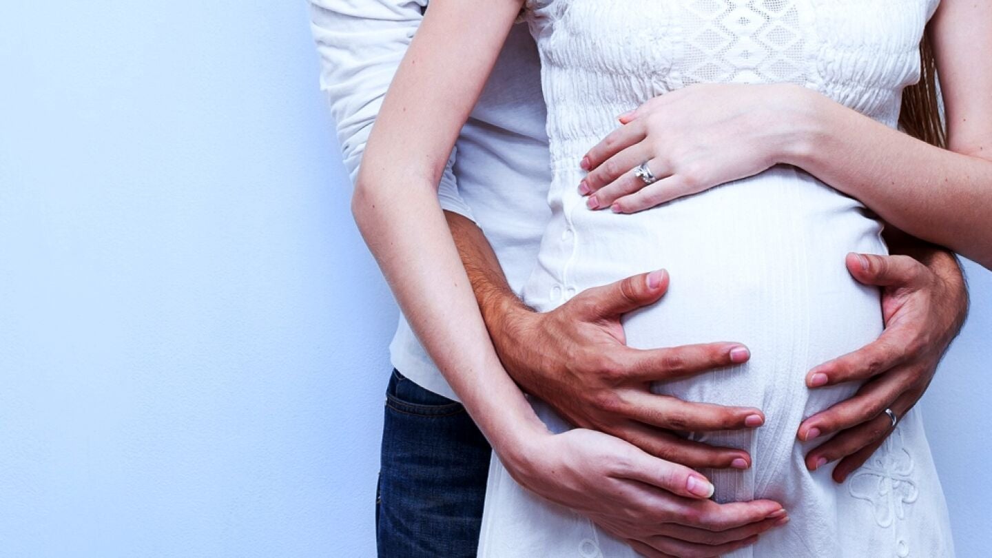 Una mujer embarazada con las manos de un hombre sobre su barriga