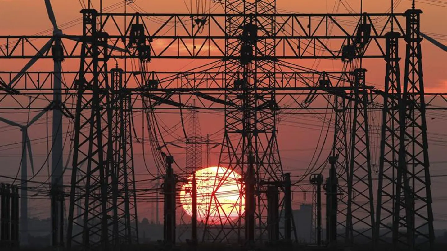En la imagen, una puesta de sol junto a un tendido eléctrico y unos molinos de viento En la imagen, una puesta de sol junto a un tendido eléctrico y unos molinos de viento