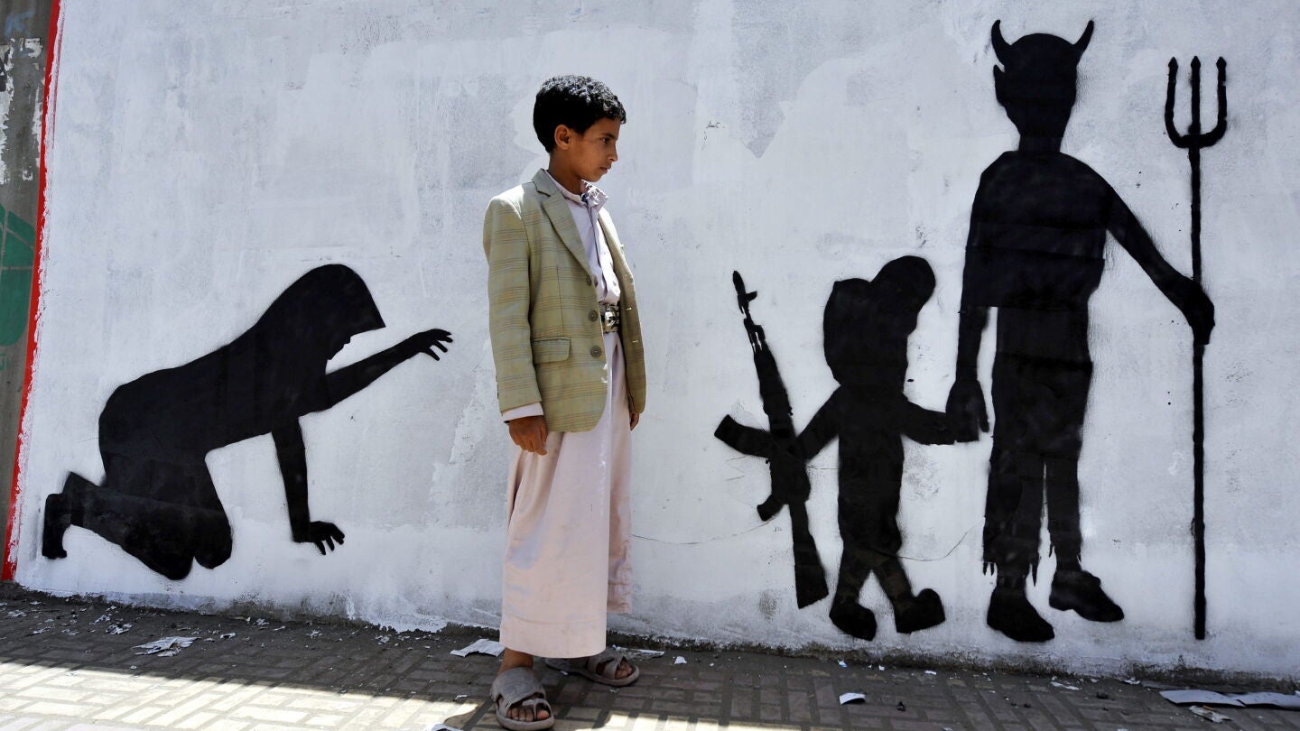Un ni&ntilde;o yemen&iacute; observa el grafiti de la pared en la que se muestra a un ni&ntilde;o soldado caminando de la mano de un demonio