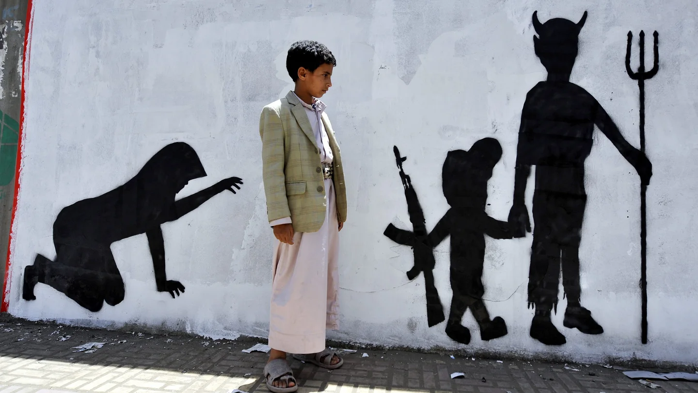 Un niño yemení observa el grafiti de la pared en la que se muestra a un niño soldado caminando de la mano de un demonio Un niño yemení observa el grafiti de la pared en la que se muestra a un niño soldado caminando de la mano de un demonio