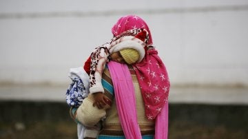 Una mujer lleva en brazos a su hijo bajo la lluvia en Srinagar (India)