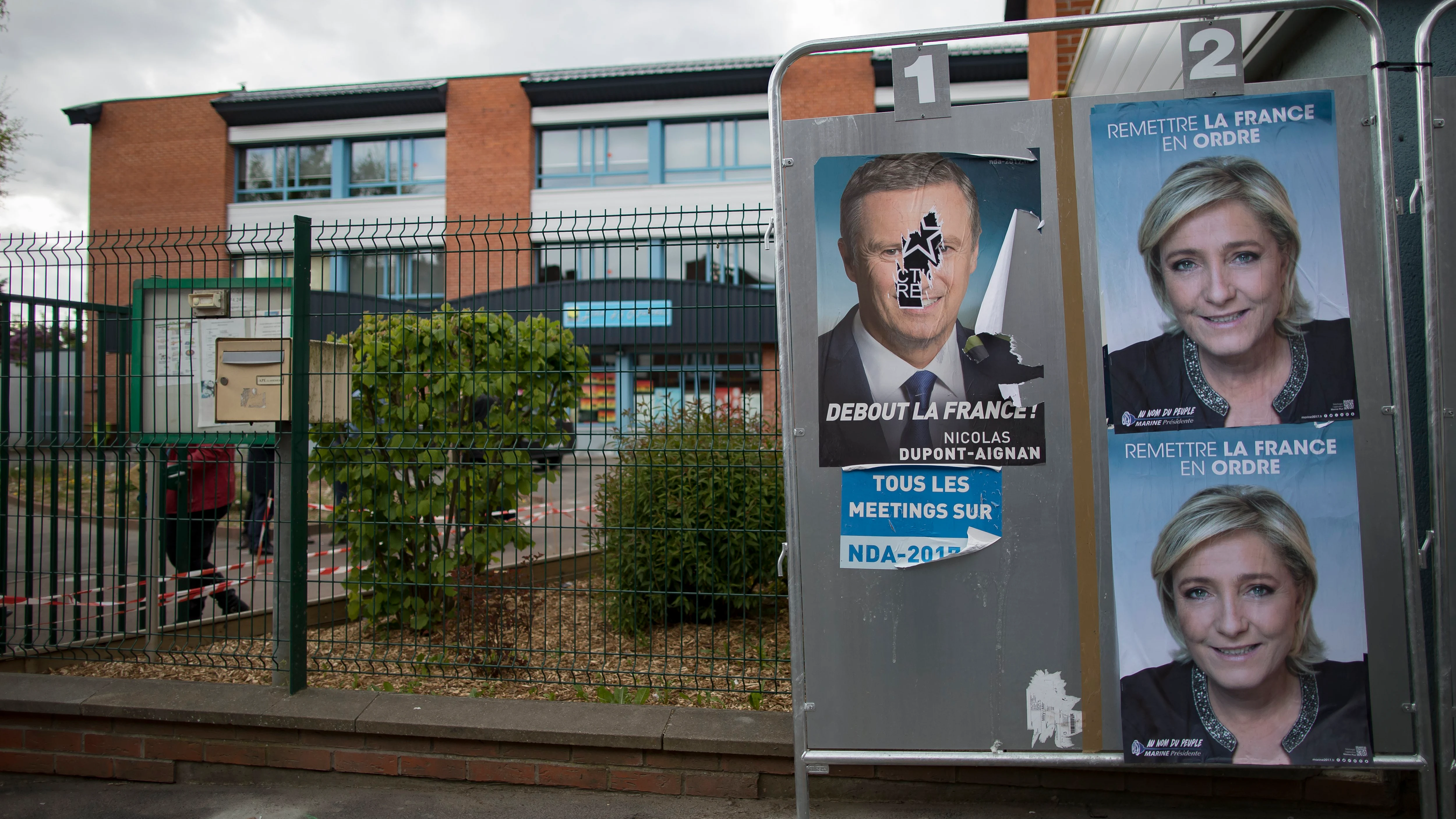 Carteles con alguno de los candidatos presidenciales en Francia adornan vallas publicitarias en el exterior de una mesa electoral en París (Francia)