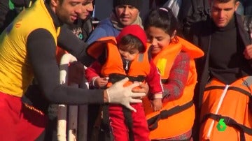 Un voluntario ayuda a un grupo de refugiados a llegar a tierra