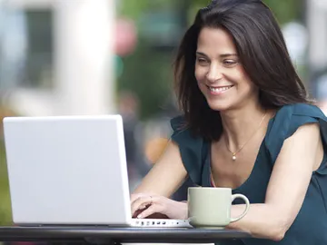 Una chica mira su portátil con una taza Una chica mira su portátil con una taza